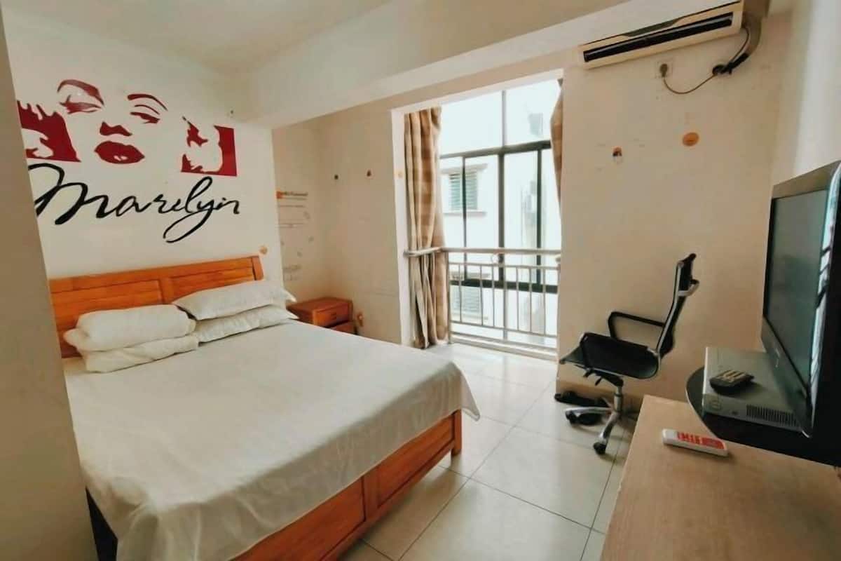 A hotel room with a bed, a desk with a television, a chair, and a window with curtains.