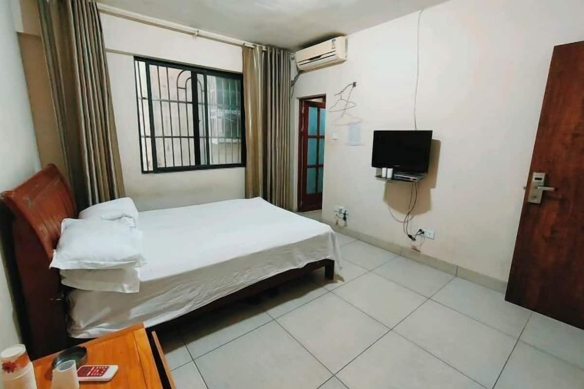 A bedroom with a bed, a TV mounted on the wall, an air conditioning unit, and a wooden door.