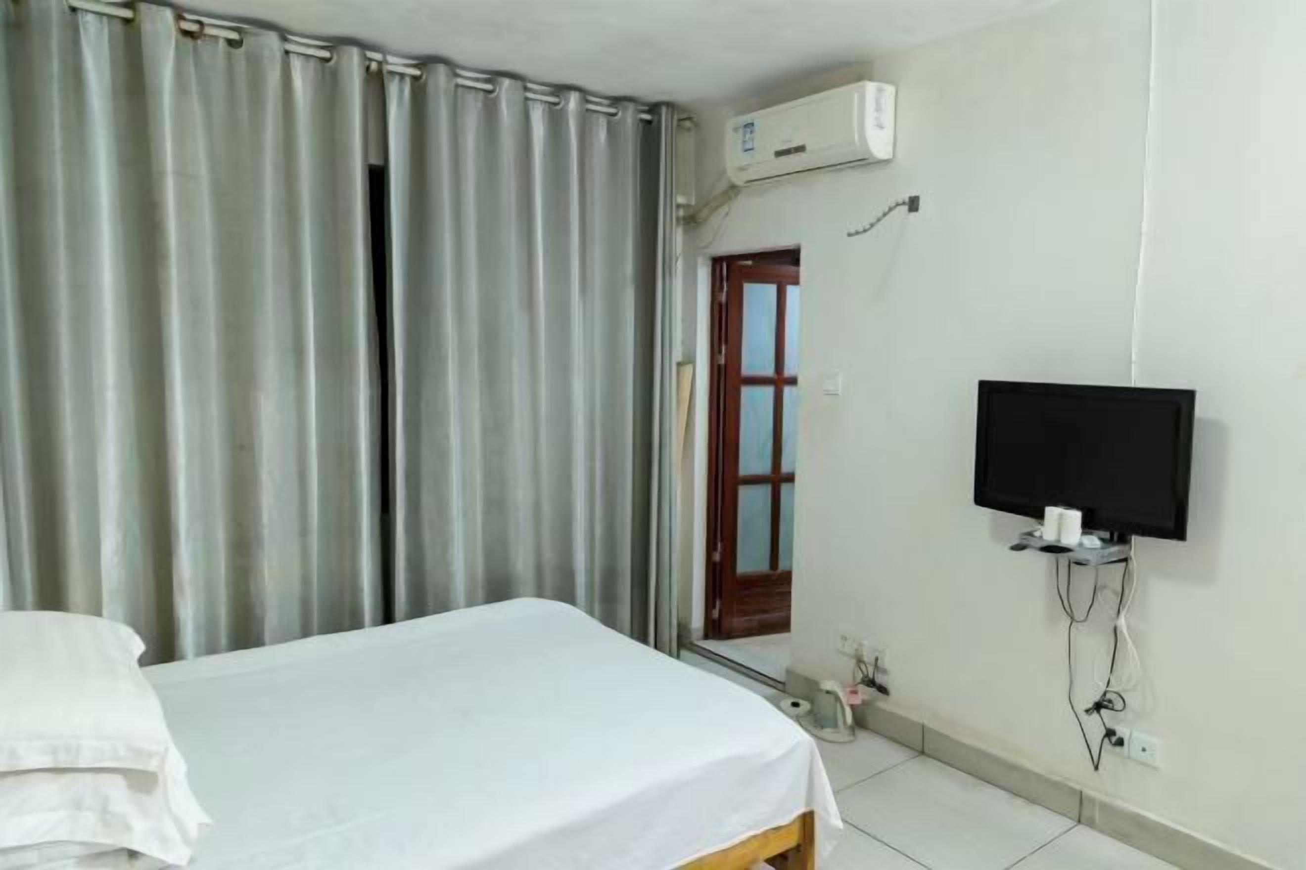 A hotel room with a bed, curtains, an air conditioning unit, a television, and a door leading to a balcony.