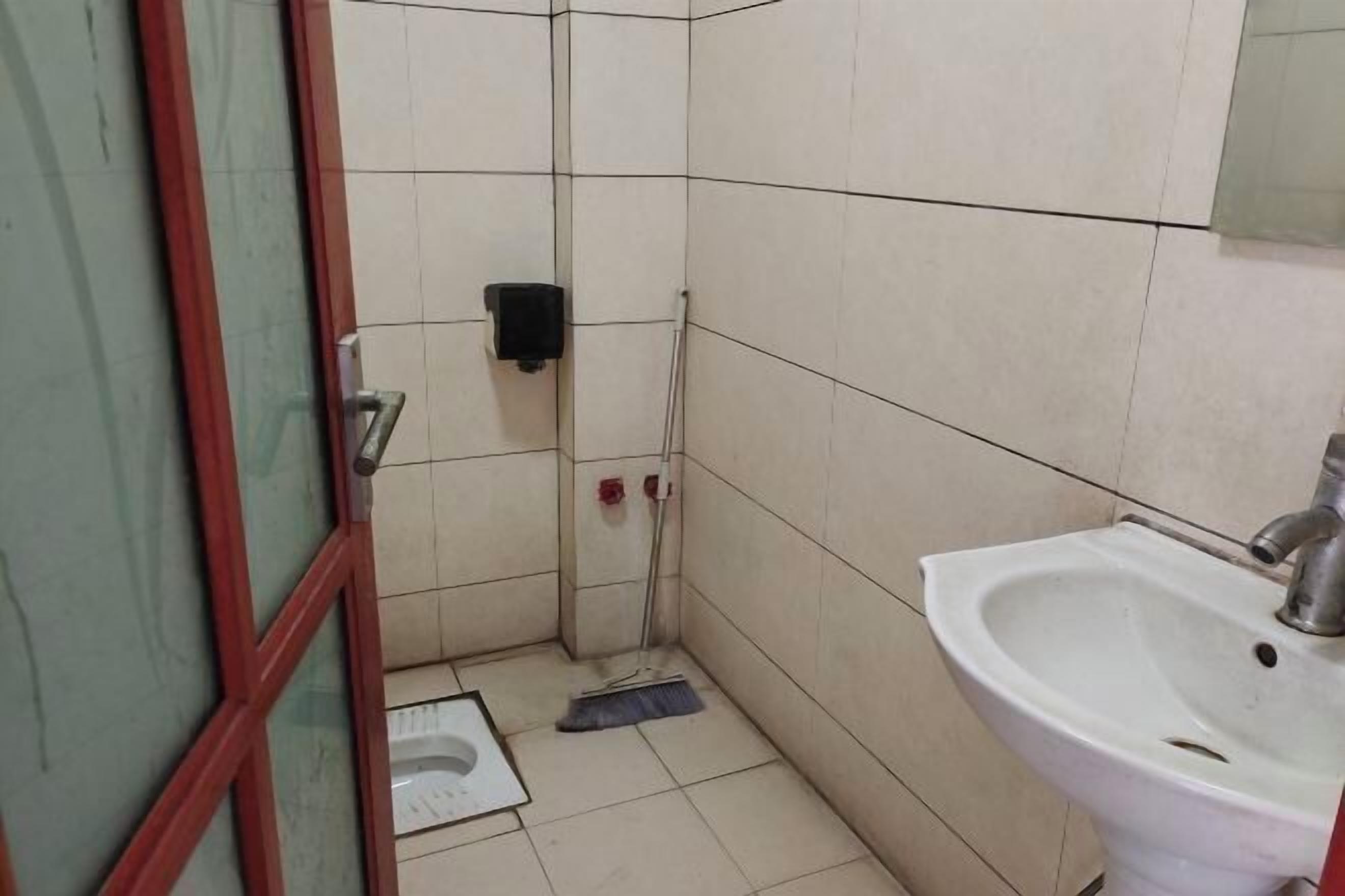 Une petite salle de bain avec des toilettes, un lavabo et un balai appuyé contre le mur.
