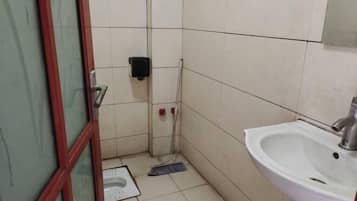 Une petite salle de bain avec des toilettes, un lavabo et un balai appuyé contre le mur.