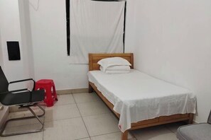 A small, clean room with a single bed, a chair, and a red stool. - Sanya Qingyi Bay Hotel (Sanya)