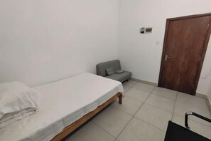 A small, clean room with a single bed, a grey sofa, a wooden door, and a chair. - Sanya Qingyi Bay Hotel (Sanya)