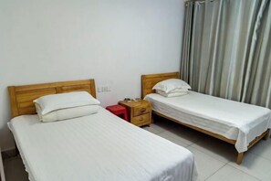 A small, clean room with two single beds, a wooden nightstand, and a red stool. - Sanya Qingyi Bay Hotel (Sanya)