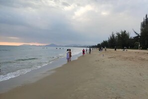 A beach with a sandy shore, trees, and a cloudy sky. - Sanya Qingyi Bay Hotel (Sanya)