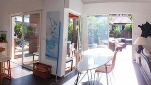 A spacious living area with a large window, a dining table, and a sofa. - Maison 130 m2 sur Jardin 600 m2 à 900 m de la Plage et Centre Ville-4 Chambres (Lacanau)