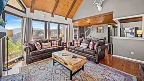 A spacious living room with two brown leather sofas, a wooden coffee table, and large windows offering a mountain view.