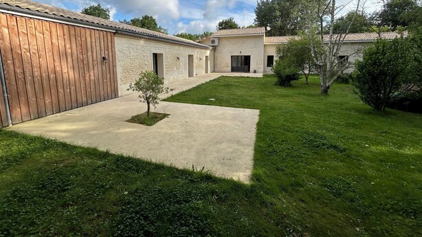 A building with a wooden exterior and a small tree in the center. - Maison Proche lac Hourtin et Océan (Gaillan-en-Médoc)