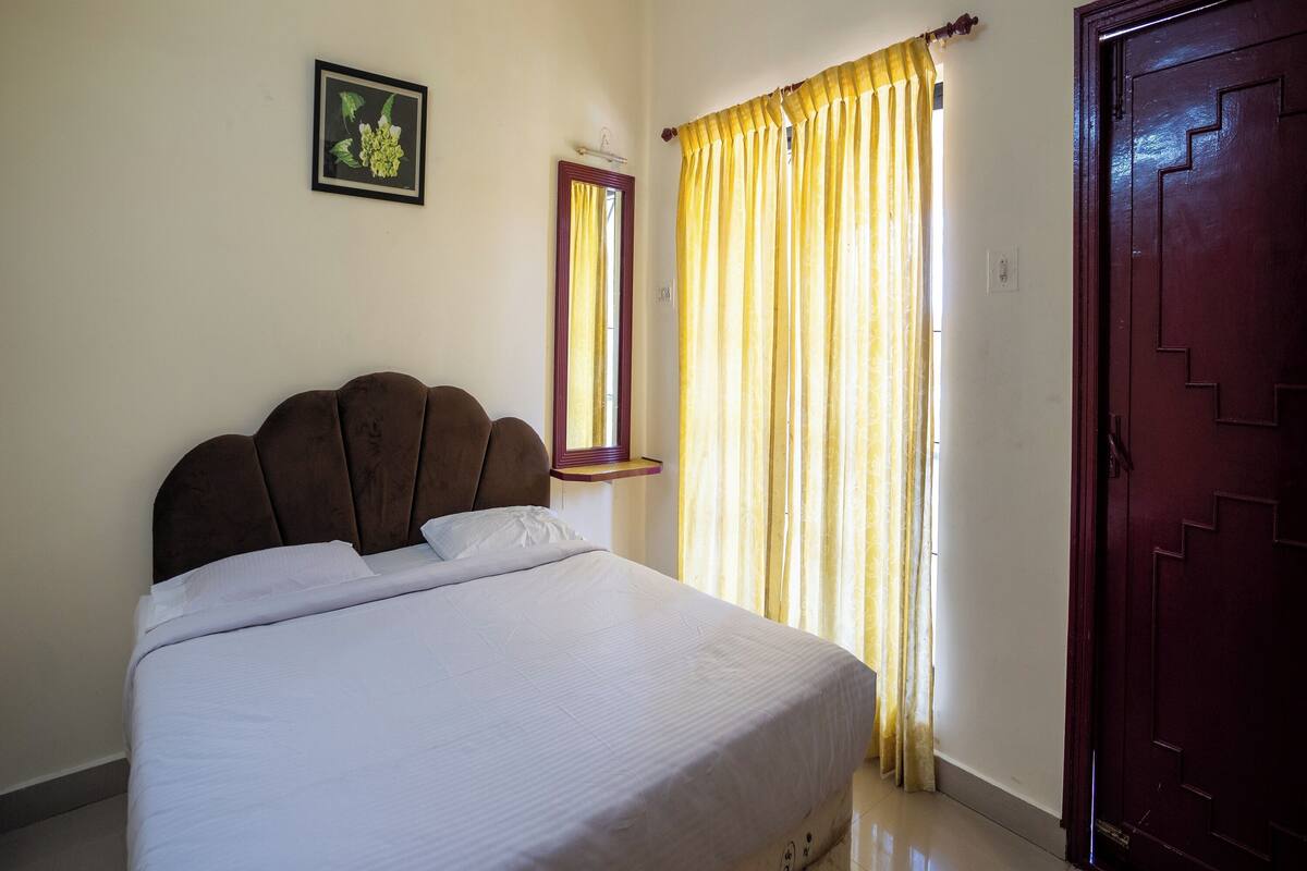 A bedroom with a bed, a window with curtains, a door, and a framed picture on the wall.