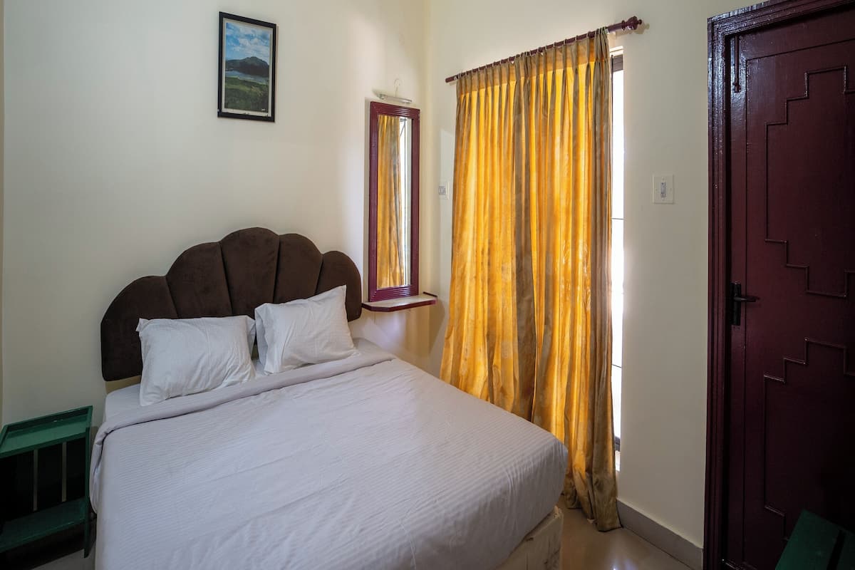 A bedroom with a bed, a window with yellow curtains, a door, and a framed picture on the wall.