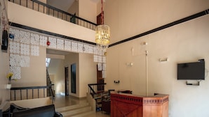 A spacious lobby with a black leather sofa, a wooden reception desk, and a staircase leading to an upper level.