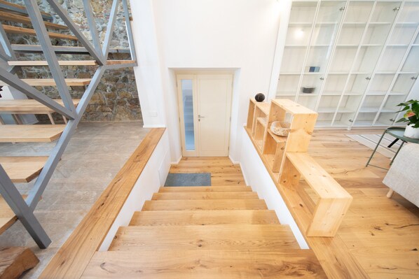 A wooden staircase leading to a door, with a stone wall and a glass shelving unit in the background.