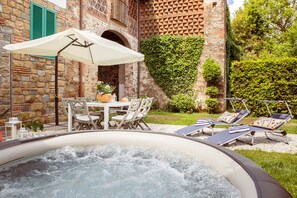 A hot tub with a table and chairs, a lounge area with sunbeds, and a stone building with a green wall.