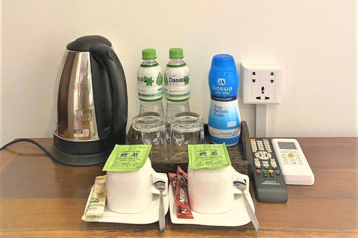A table with a kettle, Dasani water bottles, a blue water bottle, a power strip, a phone, and packets of Japanese green tea.