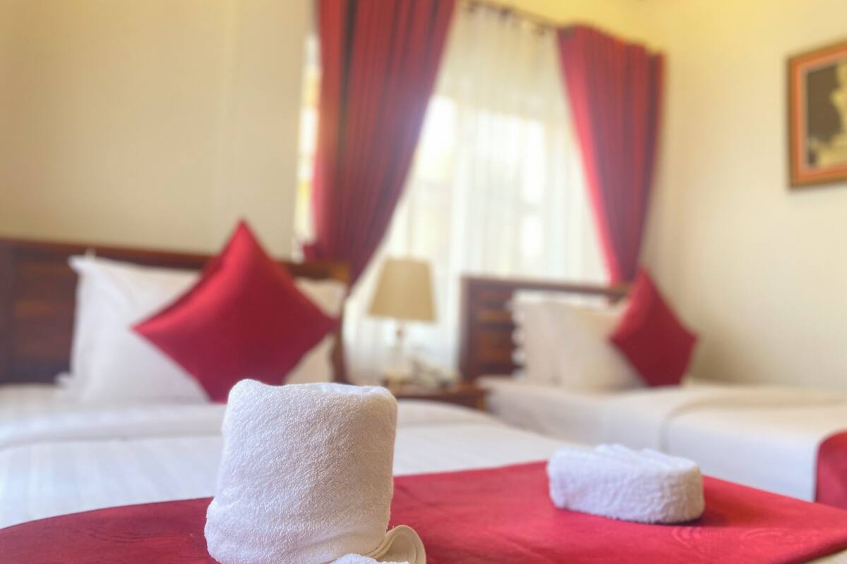 A hotel room with two beds, red curtains, white towels, and a painting on the wall.
