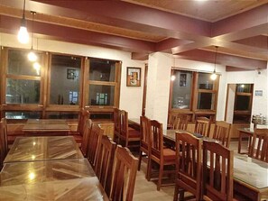 A restaurant with wooden tables and chairs, large windows, and hanging light fixtures.