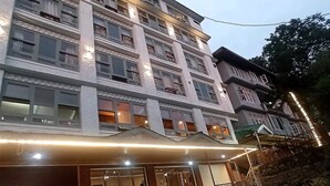 Un hôtel à plusieurs étages, avec une rangée de balcons à chaque étage, une entrée couverte et un mur de pierre sur le côté droit.