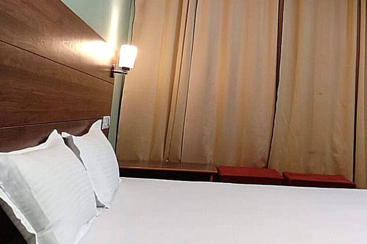 A hotel room with a bed, a nightstand, a lamp, and a window with curtains.
