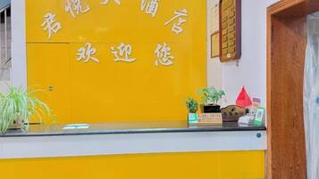 A reception desk with a yellow and white color scheme, a wooden door to the right, and a small plant on the counter.