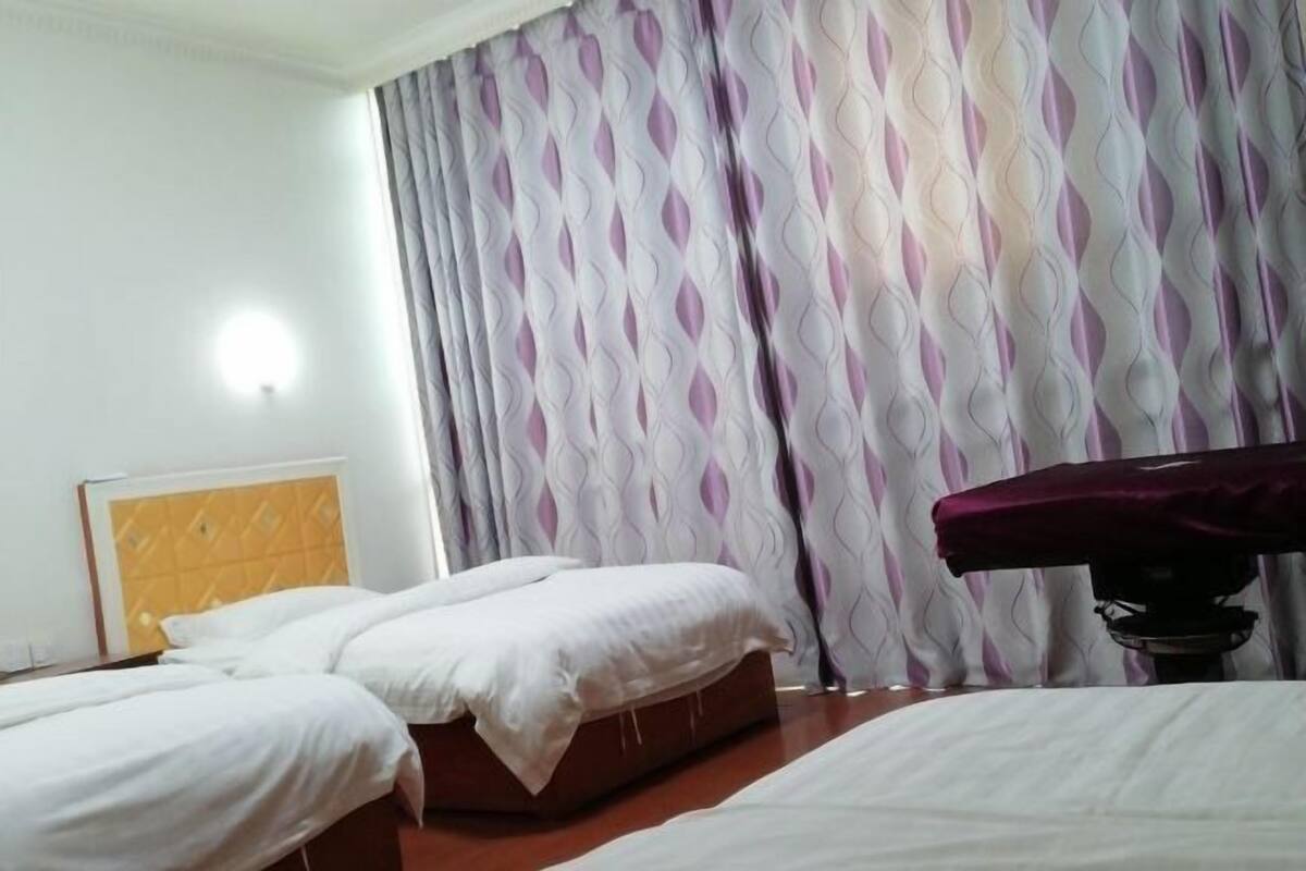 A hotel room with two beds, a headboard, a bedside table, and a curtain with a geometric pattern.