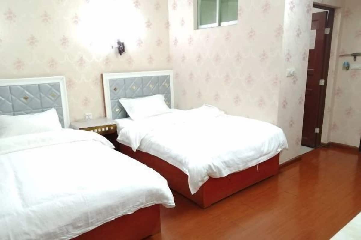A room with two beds, wooden flooring, and floral wallpaper.