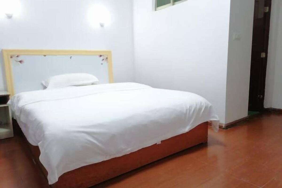 A single-bed room with a wooden headboard, white bedding, and a small bedside table.