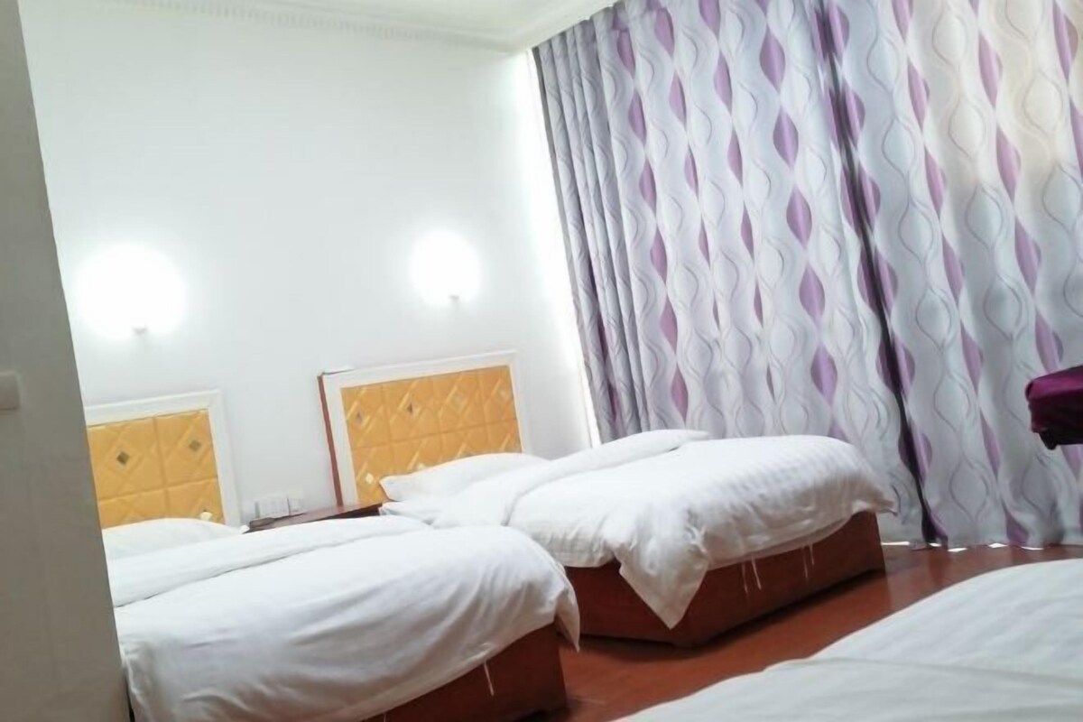 A hotel room with two beds, a yellow headboard, white bedding, and patterned curtains.