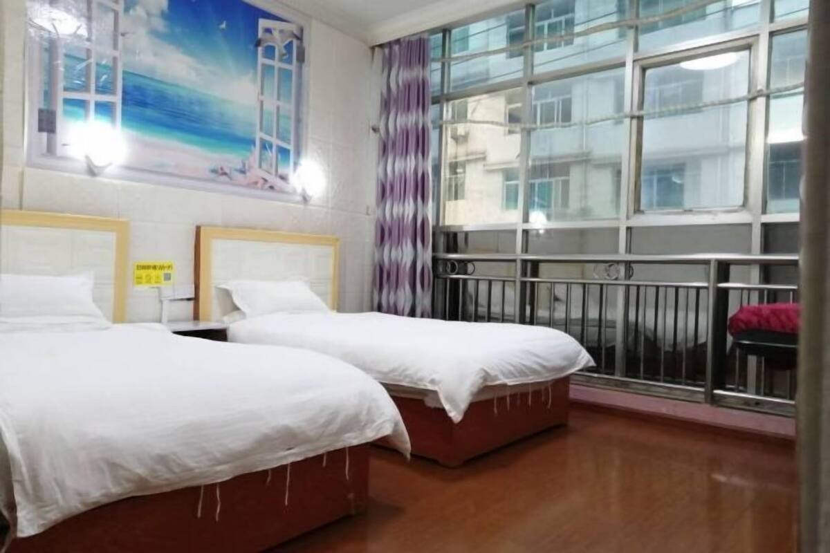 A hotel room with two beds, a large window with a view, and a balcony with a railing.