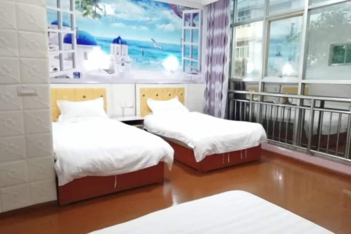 A hotel room with two beds, a large window with a view of the sea, and a mural of a coastal scene.
