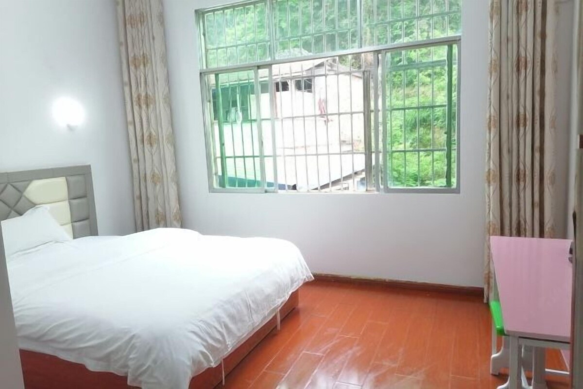 A room with a bed, a window with metal bars, a small table, and a chair.