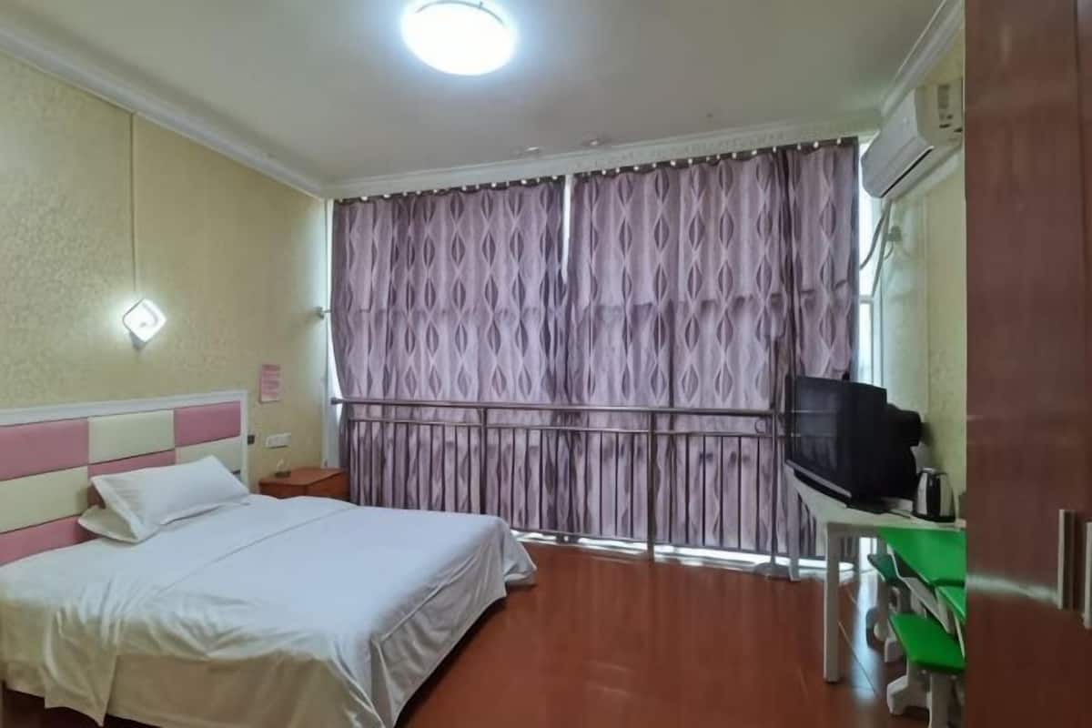 A hotel room with a bed, a nightstand, a TV, and a window with curtains.