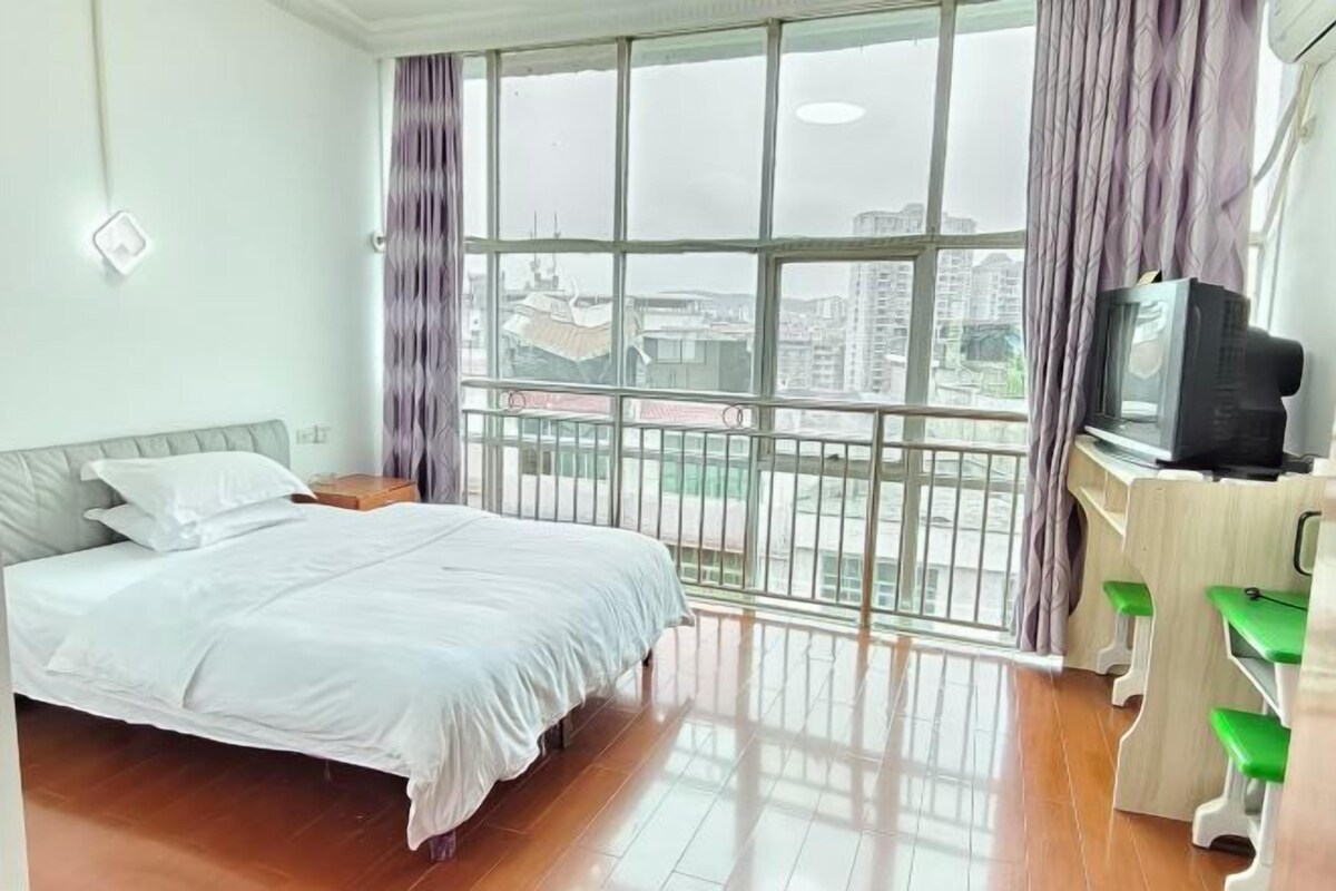 Habitación de hotel con cama, escritorio con televisor y vistas amplias a través de grandes ventanales.