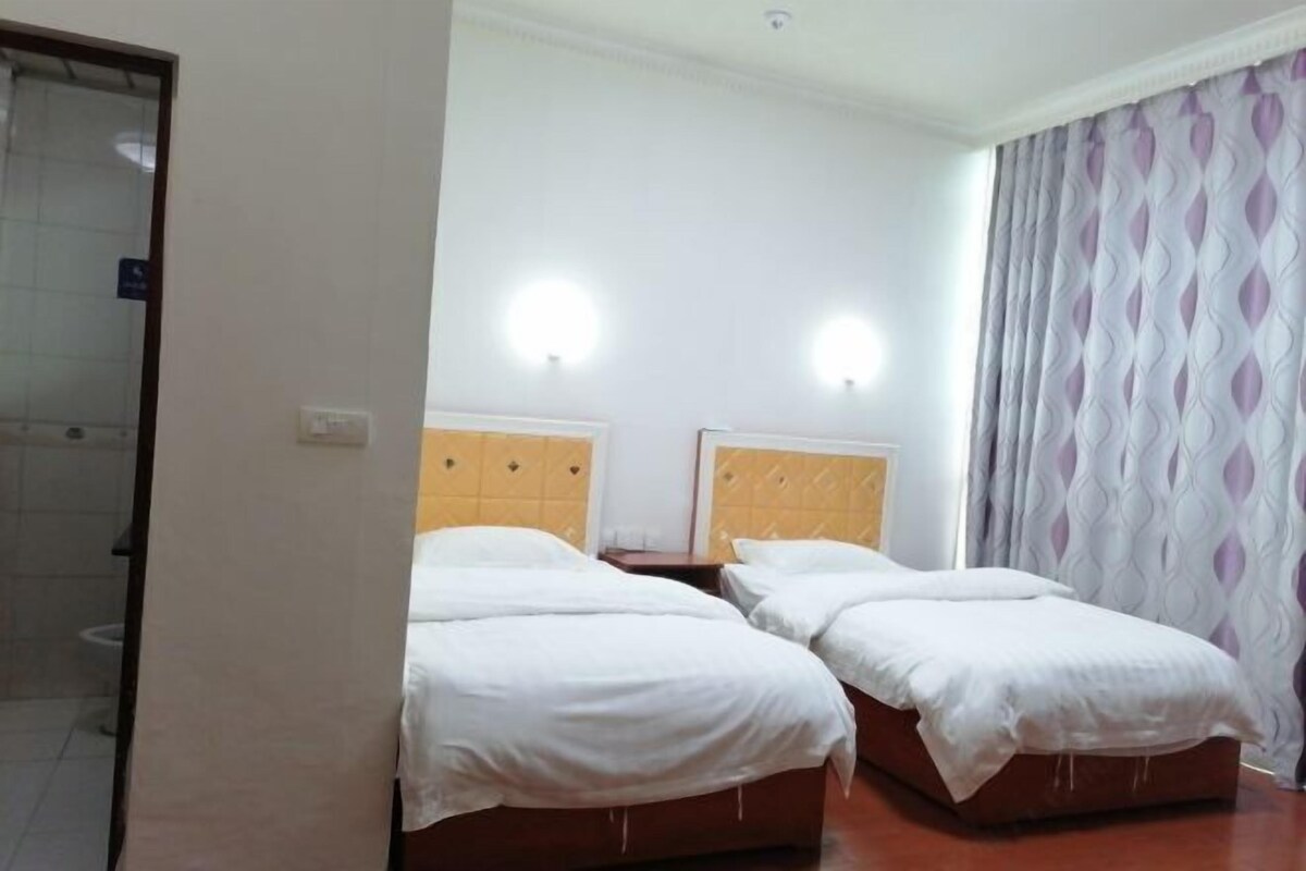A hotel room with two beds, a wooden headboard, a white wall, and a patterned curtain.