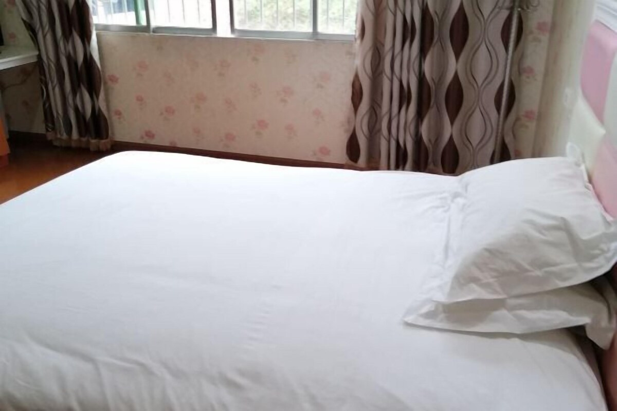 A bedroom with a bed, floral wallpaper, and curtains.