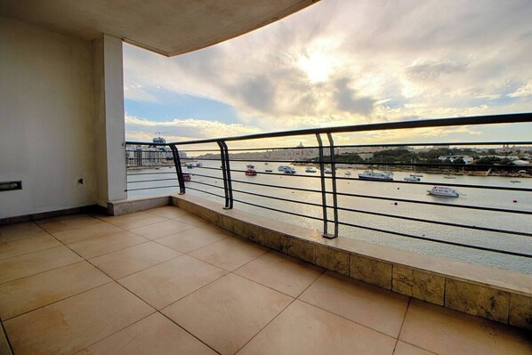 A balcony with a view of a harbor, featuring boats and a bridge.