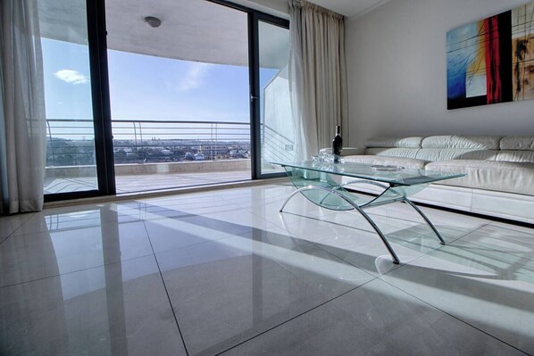 A modern living room with a glass coffee table, a white sofa, and a large sliding glass door leading to a balcony with a city view. - Enjoy a stylish stay just steps from Sliema Ferries! Spacious apartment for up to 8 guests with stunning harbour views — perfect for a relaxing Malta getaway (Tas-Sliema)