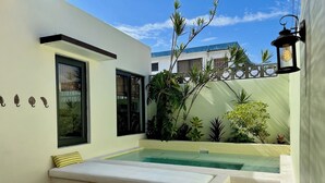Un área de piscina exterior moderna con un banco integrado, una pequeña mesa y una escalera que conduce a un porche cubierto.
