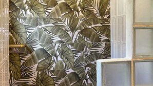 Un baño con un diseño de hojas tropicales en la pared, una ducha con reposacabezas negro y mampara de vidrio.