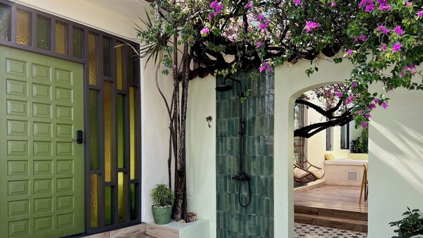 Una puerta verde con teclado, un patio empedrado con suelo estampado y una zona de estar con mesa y sillas.