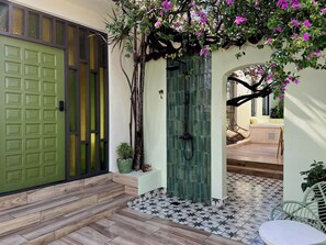 Una puerta verde con teclado, un patio empedrado con suelo estampado y una zona de estar con mesa y sillas.