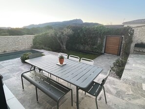 Un patio al aire libre con una mesa, bancos, una piscina pequeña y vistas a las colinas.