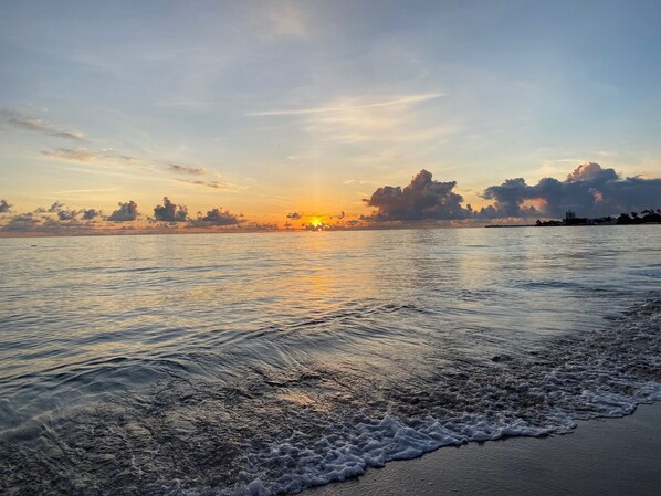A beach with calm water and a sunset in the background.