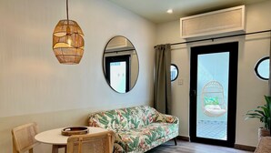 A room with a round table, two wicker chairs, a sofa with a tropical print, a hanging chair, and a potted plant.