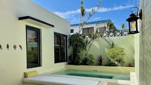 Un área de piscina exterior moderna con un banco integrado, una pequeña mesa y una escalera que conduce a un porche cubierto.