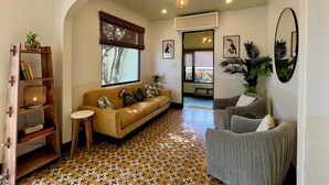 Una sala de estar con un sofá, un sillón gris, una estantería de madera, una mesita redonda y un suelo estampado.