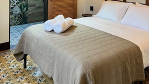 Una habitación de hotel con una cama, un ventilador de techo, una mesita de noche y una puerta con un cerrojo de madera.