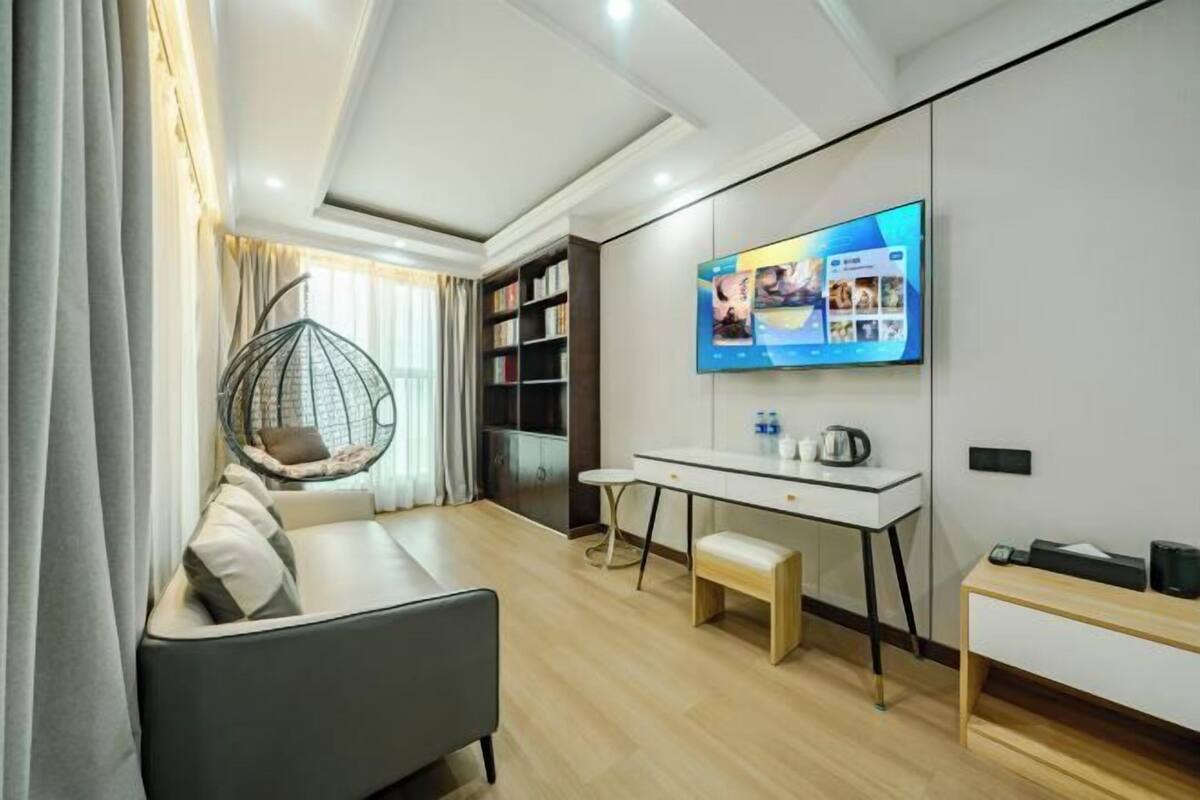 A modern living room with a sofa, a hanging chair, a desk, and a flat-screen TV mounted on the wall.