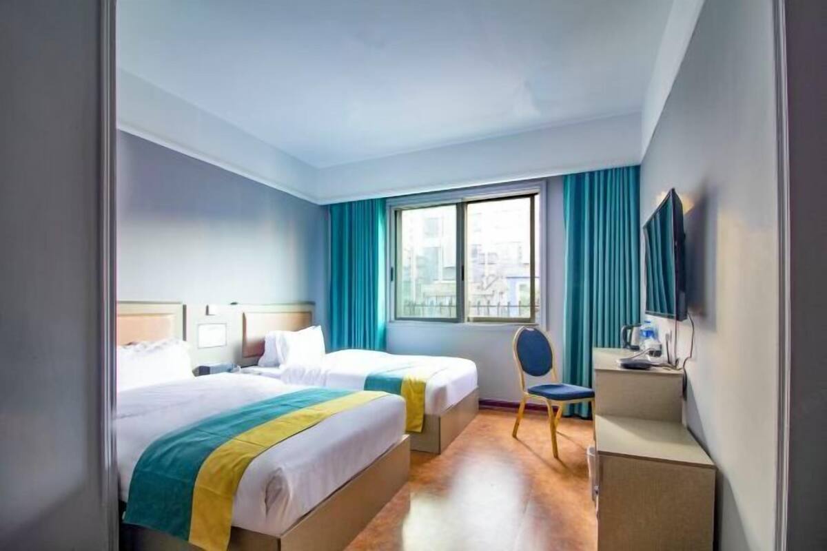 A hotel room with two beds, a desk, a chair, a TV, and a window with curtains.