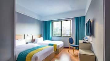 Habitación de hotel con dos camas, un escritorio, una silla, un televisor y una ventana con cortinas.