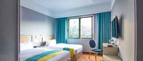 Habitación de hotel con dos camas, un escritorio, una silla, un televisor y una ventana con cortinas.